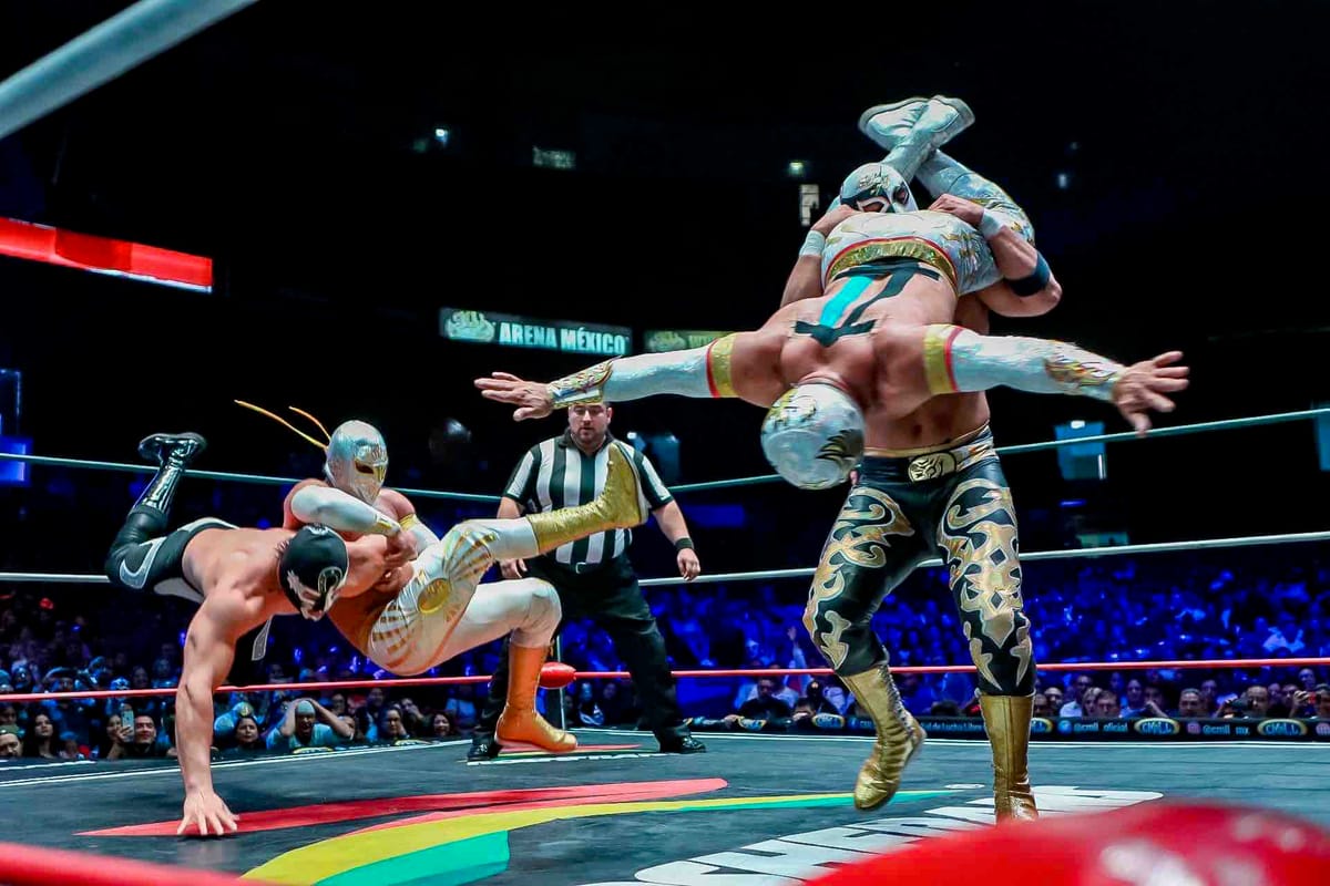 Lucha Libre wrestling featuring two pairs of wrestlers and a referee in a ring in front of a large crowd